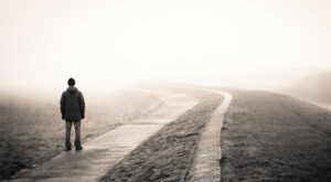 A man looks down a road on a day with poor visibility due to fog
