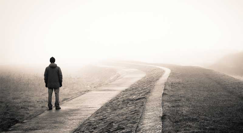 A man looks down a road on a day with poor visibility due to fog