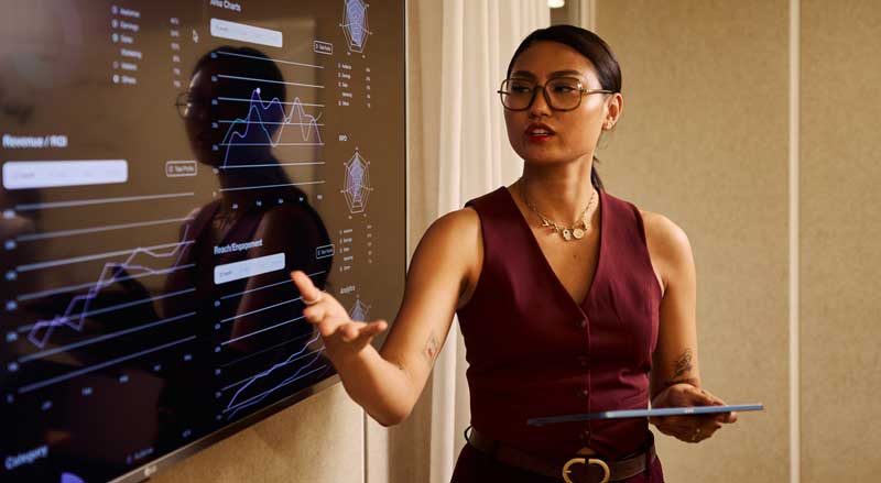 Marketing professional presenting growth analytics and performance data on a large screen during a strategy discussion
