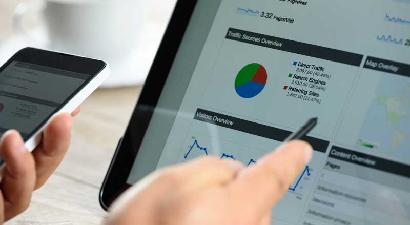 Person reviewing analytics dashboard on tablet and phone showing traffic and performance data